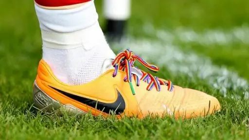 A player wears a boot laced with rainbow laces